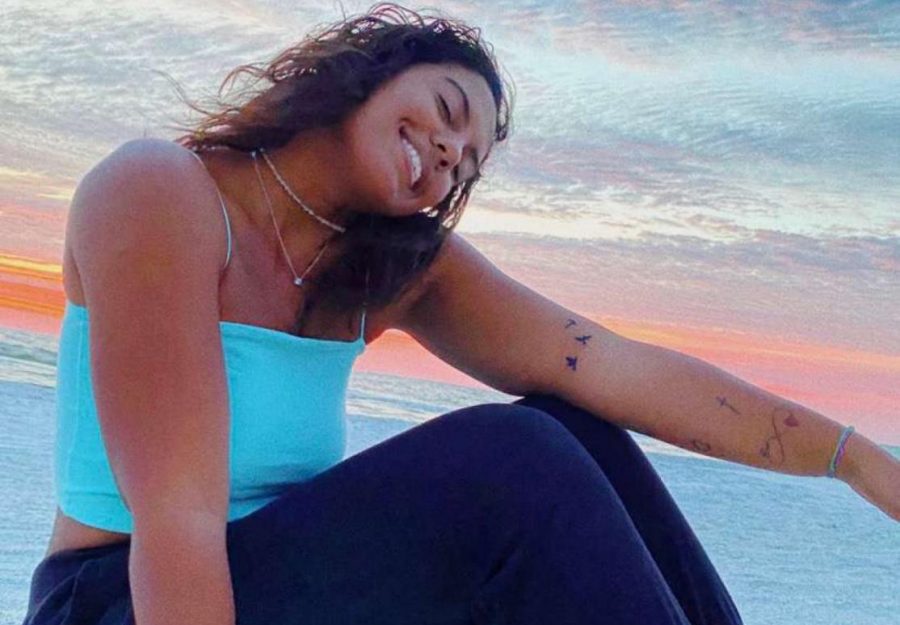 Maya Houston sitting on the beach showcasing her tattoos.