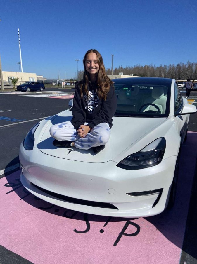 Ella Bagnuik sitting on top of her Tesla Model 3 in the Sunlake parking lot.