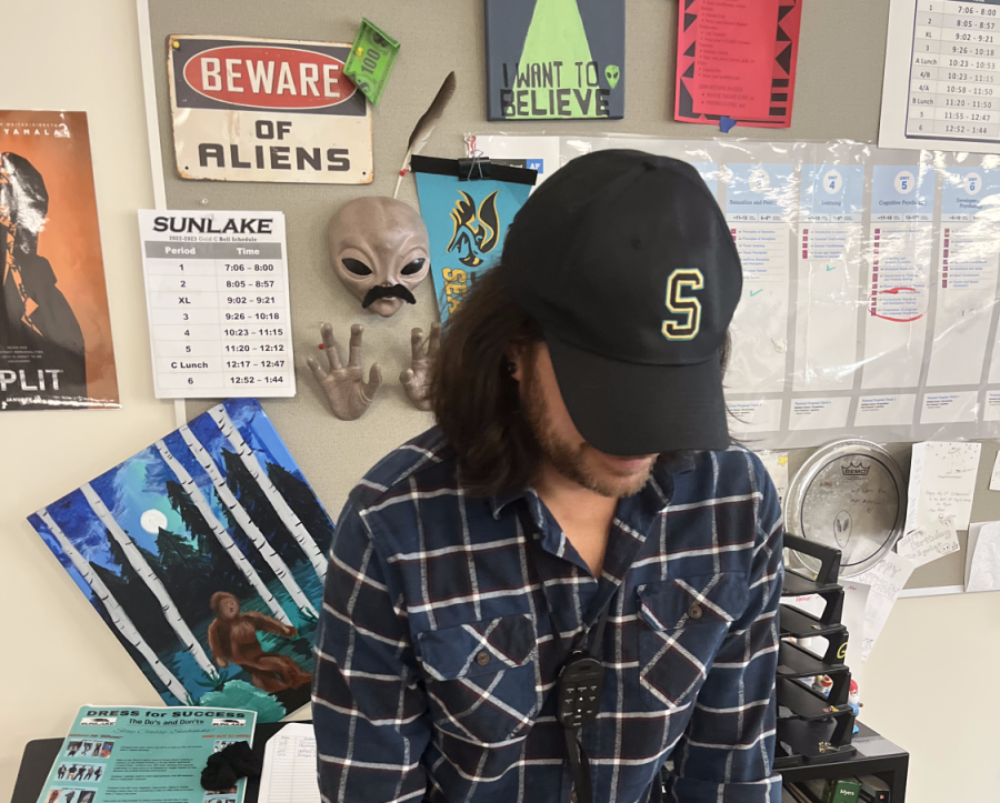 Mr. Aguiar stands in front of an alien mask, face concealed by his hat.