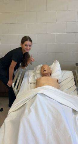 Erin Feeney, senior, next to a CPR practice dummy in the CNA classroom.