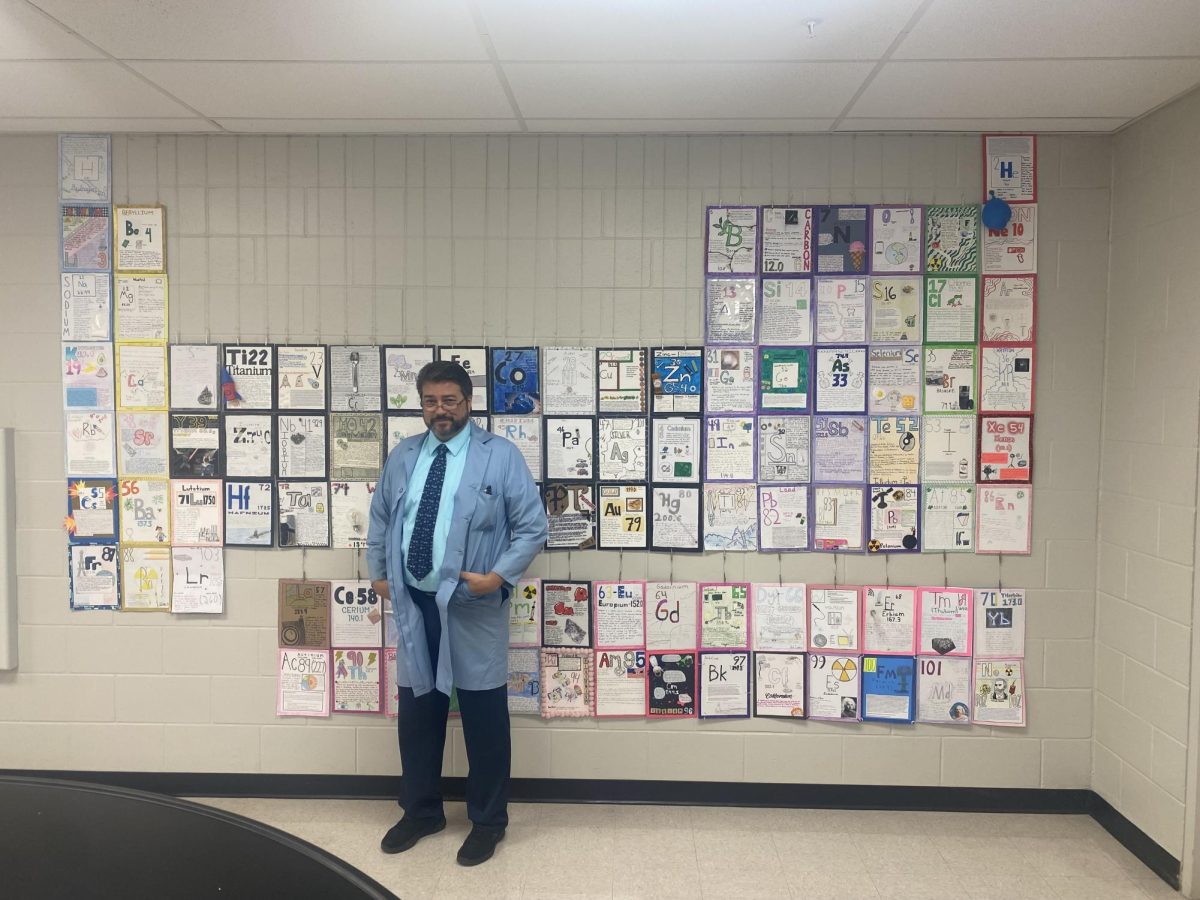 This is Mr. Maggi standing with his periodic table, which is made up of the element projects that several students worked on. He said, Some students really create some outstanding elements. Because each student has to research one element in depth, Mr. Maggi hoped ....they become an expert on their element.