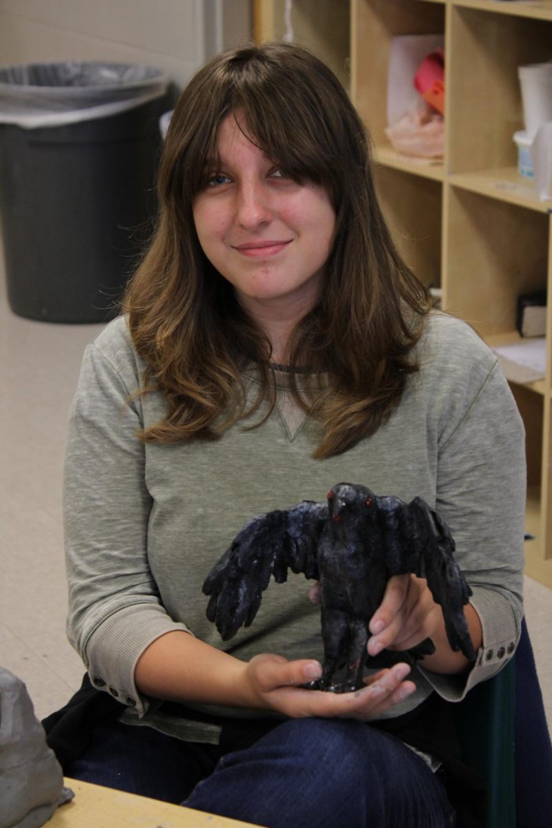 Shaylin Middleton proudly showing off her clay sculpture of a raven, based off of her projects theme of fear.