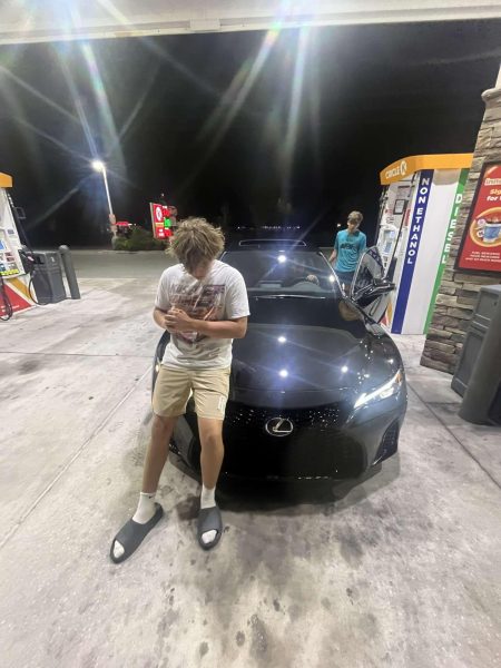 Junior Brady Lasiewski posing in front of his friend’s new car. Brady and his friends are filling the car up with gas after a drive at night.