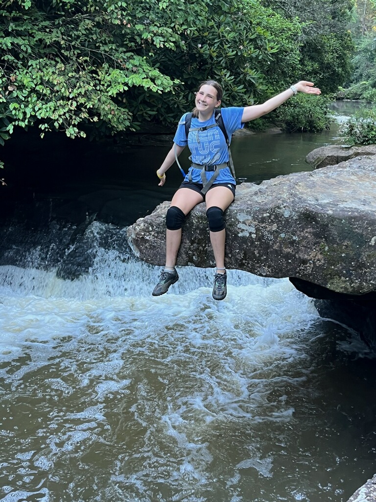 Maggie sits for a picture in front of a waterfall. She came upon this landscape while going through the mountain biking trail with her dad. She saw the beautiful scenery and knew she had to capture the moment with a picture. 