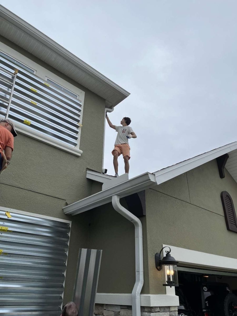 Vladyslav on top of his neighbor's house taking shutters down on the second floor, after the hurricane. Vlad said "this one was a fun one to do as I got to go on the roof and walk around up there."