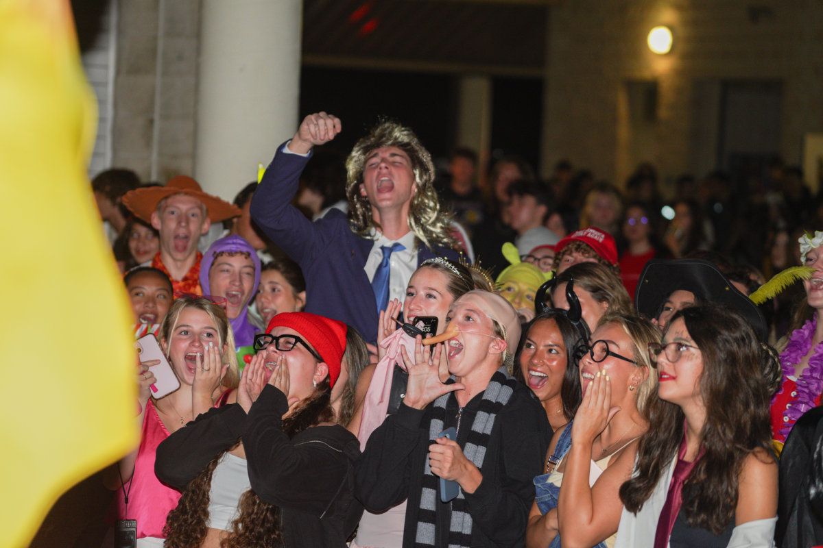 John can be seen standing in the back wearing a suit and wig while cheering loudly. Melissa can be seen standing in the front wearing the red hat also cheering. Both said that they were excited about their last homecoming week.