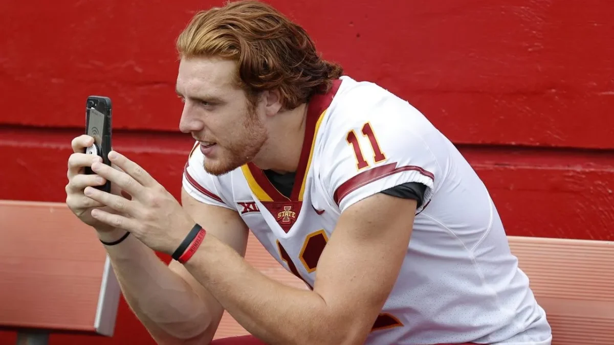 College Athlete holding phone of sideline of football field.