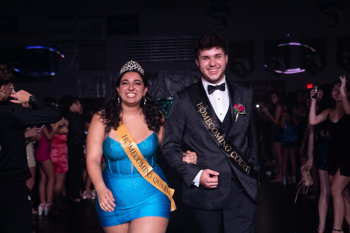 Noah walking down the aisle at the gym with his partner Lynn Raad at the Homecoming dance. They are being cheered on from both sides by all their fellow Seahawks. They are taking pride in this moment as they made it onto Hoco court their Senior Year. 