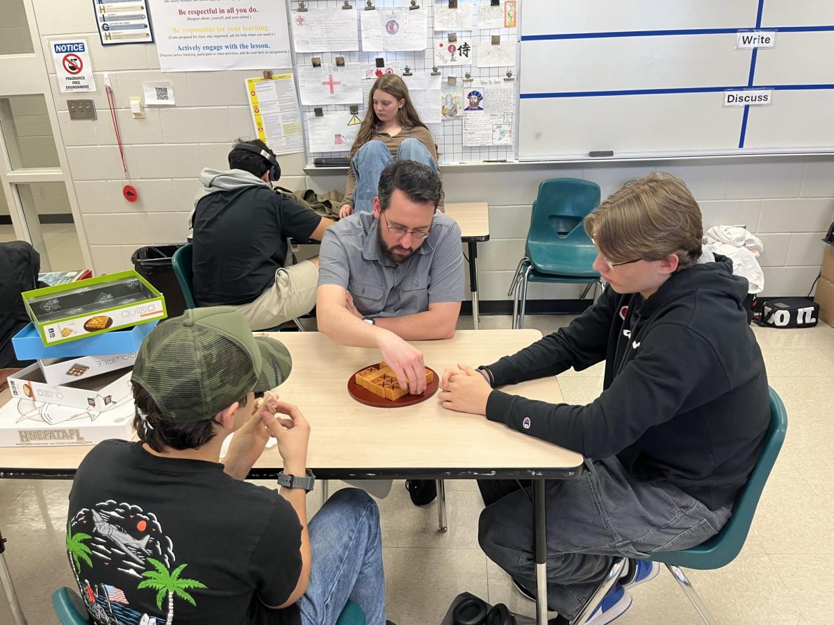 Mr. Janes  is teaching two other students in Tabletop gaming how to play Quixo.