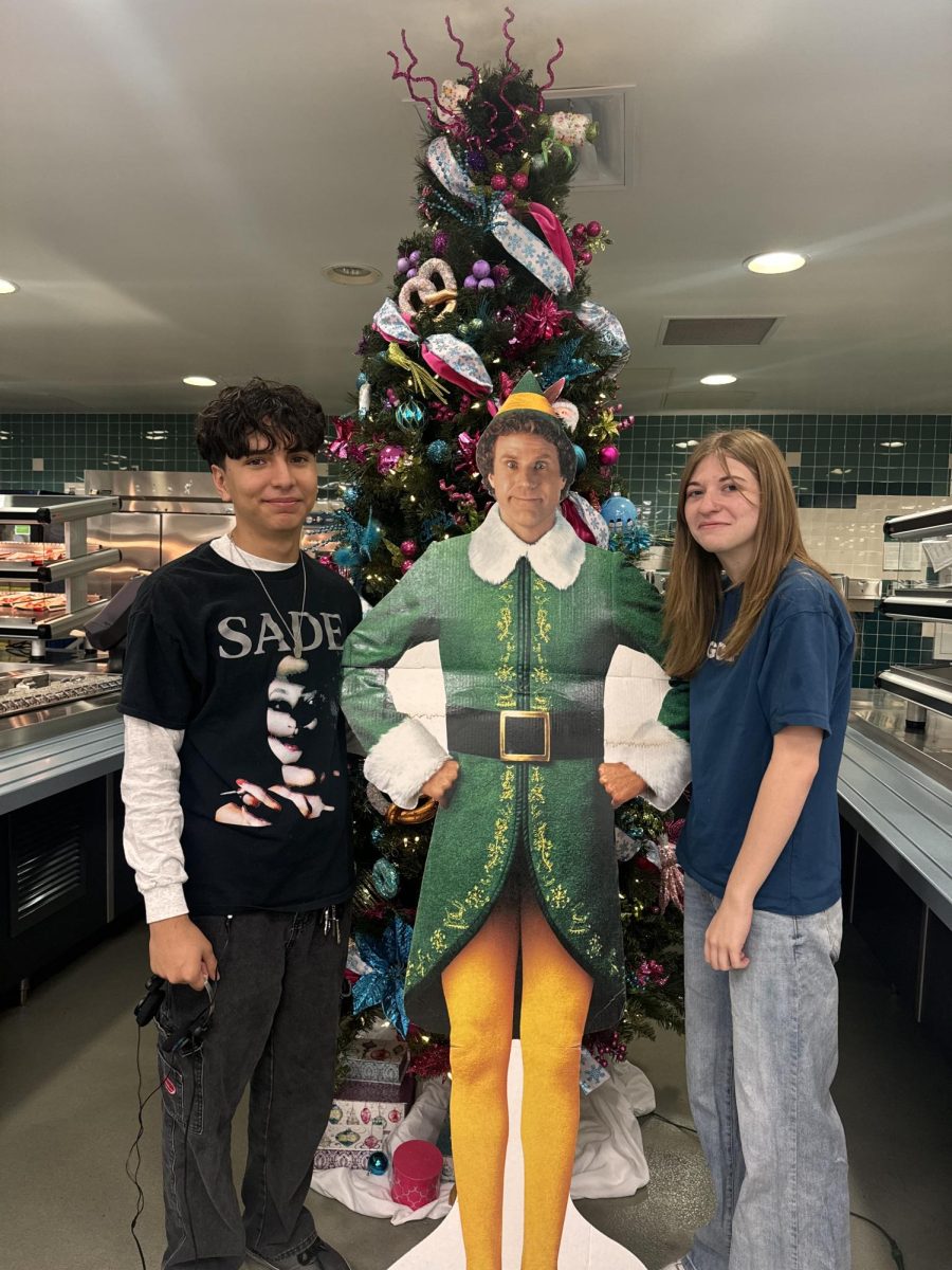 Students' Mariano Quiroga and Ava Stiglic standing in front of Buddy the Elf.