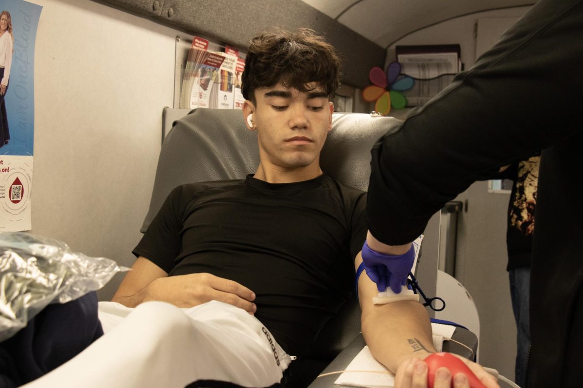 Brandon can be seen getting prepared for his blood to be taken. Brandon is happy he gets to help people out. The picture was taken on the Big Red Bus. 