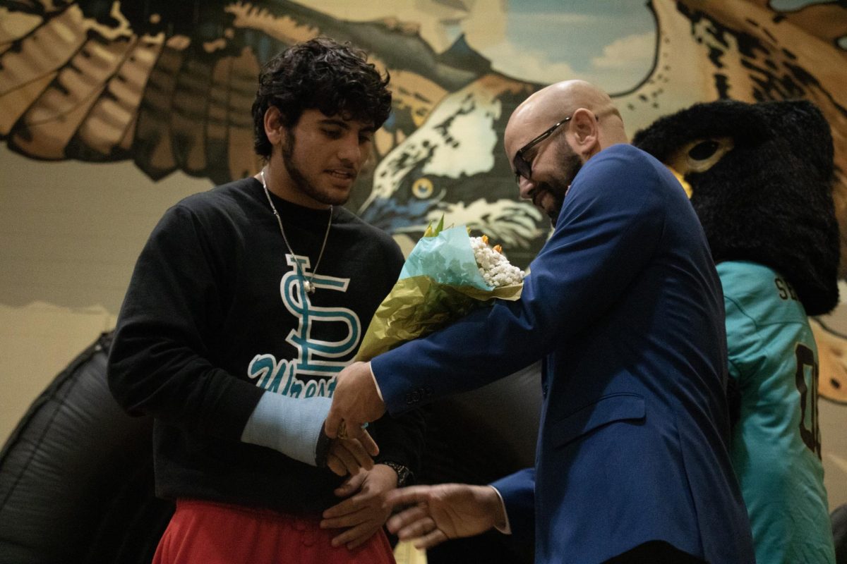 Adrien Contes receiving flowers from his wrestling coach during senior night in Sunlake's gym.