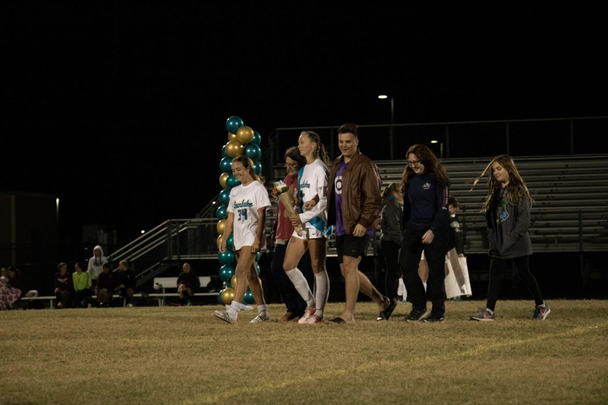 Sarah Dewey (12th) during Soccer Senior Night, walking down the field with her family.