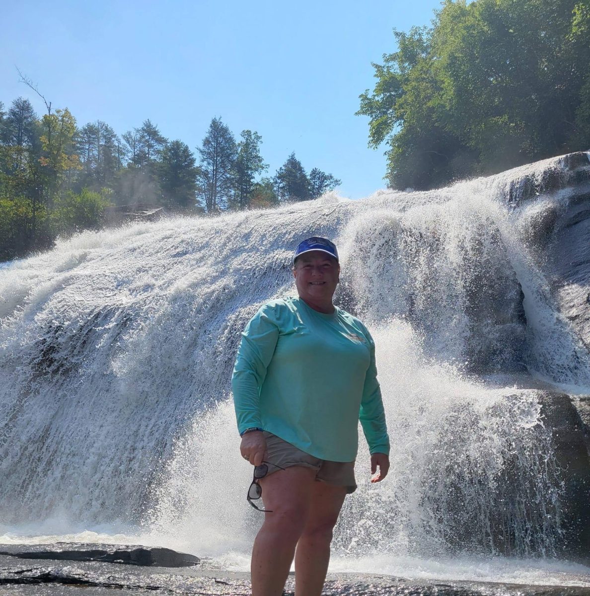 Mrs. Noffsinger on a camping trip taking a picture in front of a waterfall.