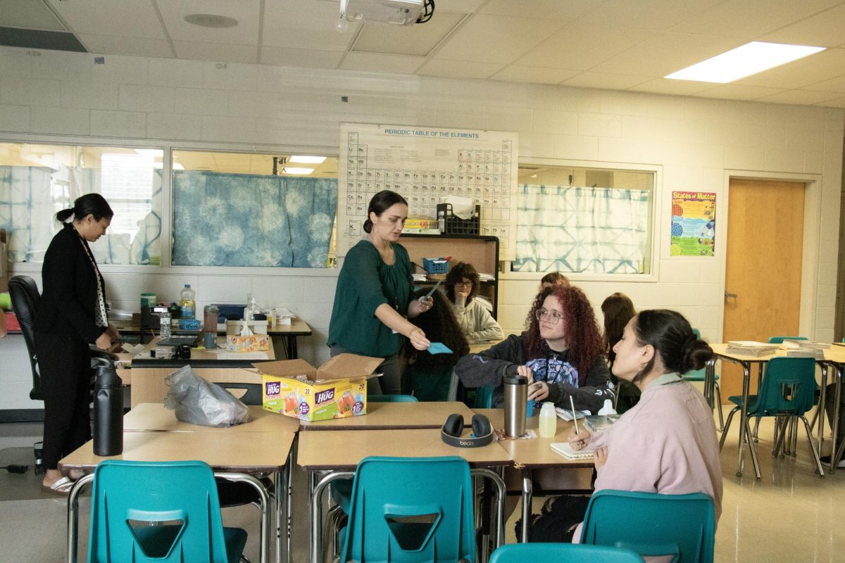 Mrs. Hale is seen in the photo. she is helping passing out things to the students who are learning from the mentor Mrs. O'Sullivan has brought in to teach about their profession.