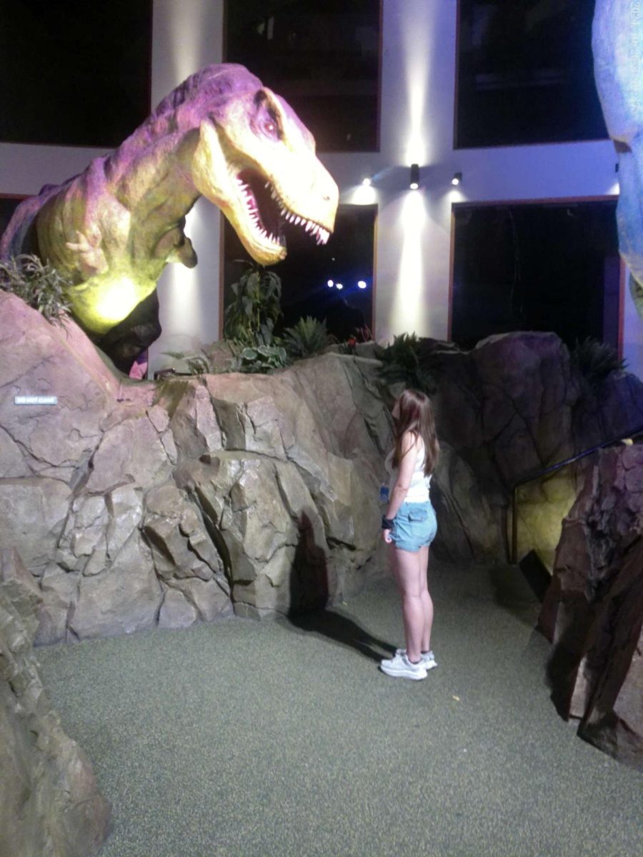 Cadyn is posing with a dinosaur. She is in line for velocicoster. She says she is "very excited."