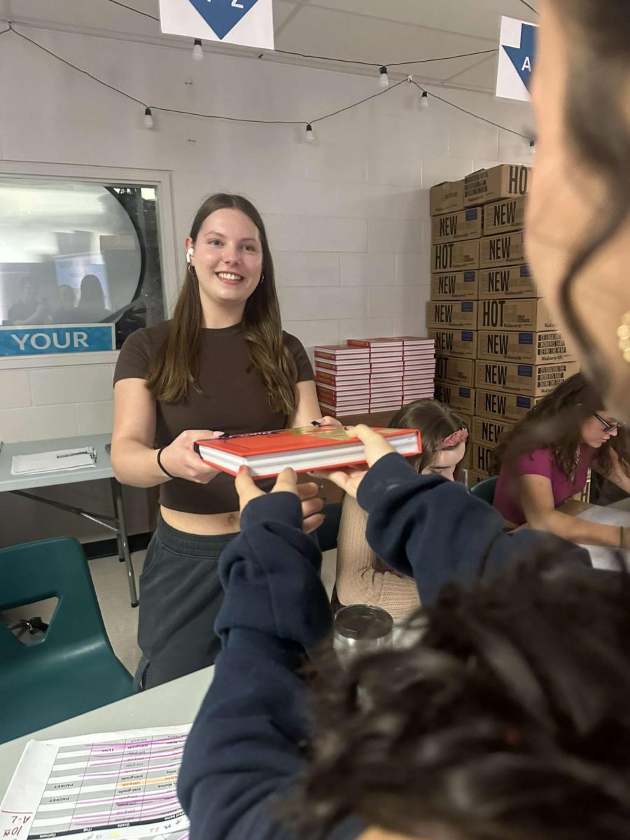 Sophomore Katie Krascka handing out a yearbook to a student Seahawk. She was excited show the student body what the yearbook staff worked on all year to create.