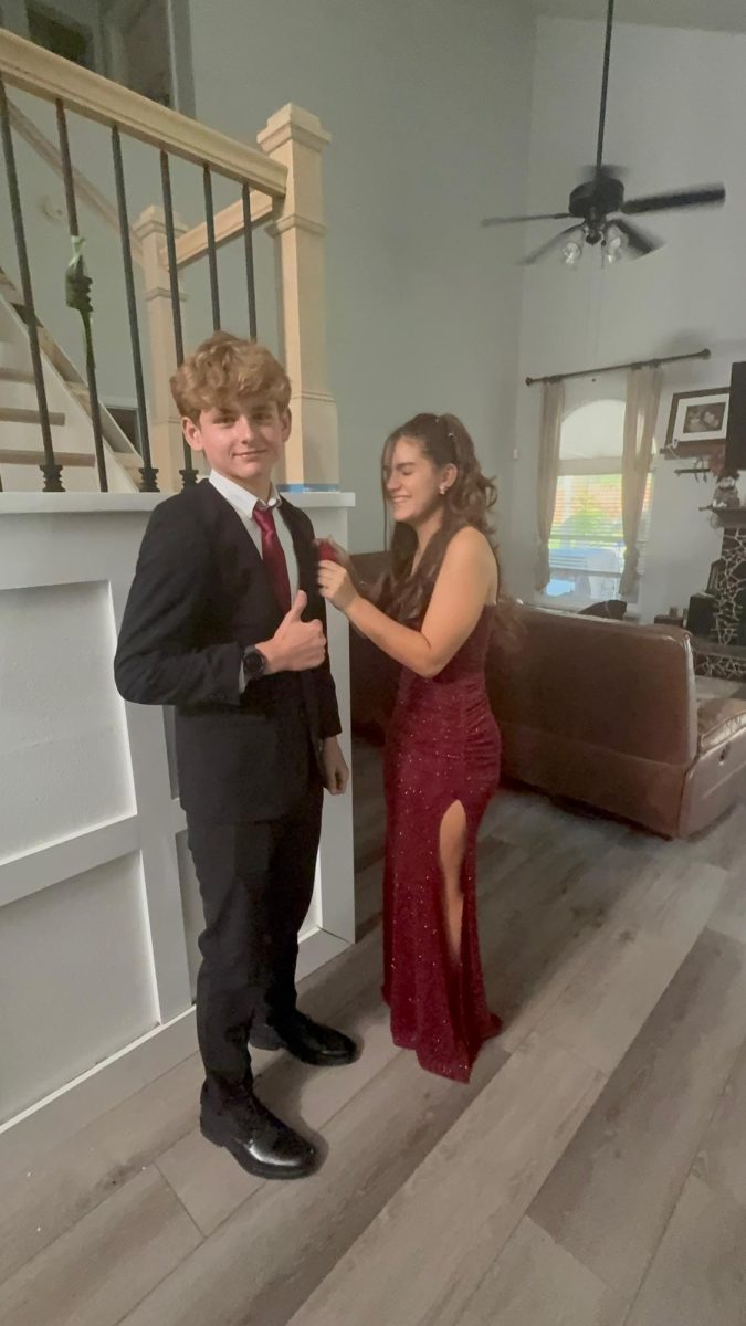Taylor and her boyfriend getting ready for homecoming, she pinning the boutonniere on him. 