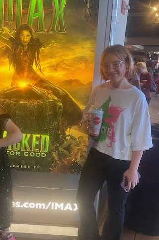 Sophomore Taylor Klus standing in front of the wicked poster excited to see the second movie. 
