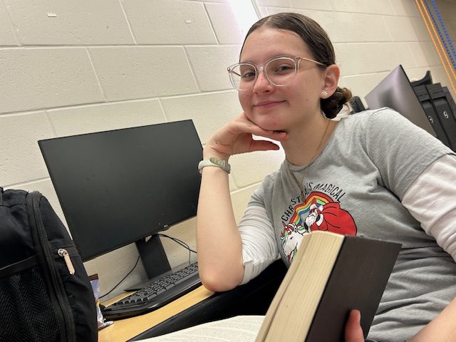 Sophomore Oriana Caldas posing with a book, sitting in front of her computer. She was ecstatic to be interviewed for this week's spirit week.