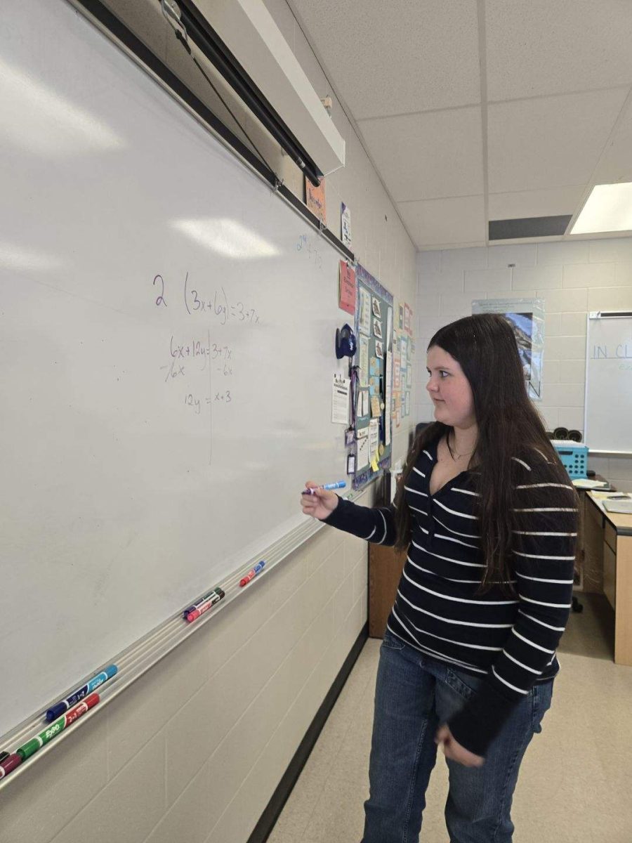 Lexi Csuhai solves a problem on the board during a Mu Alpha Theta meeting, carefully working through each step. She enjoys tackling challenging equations and explaining her thinking to others. Moments like these show her confidence in math and her leadership within the club.
