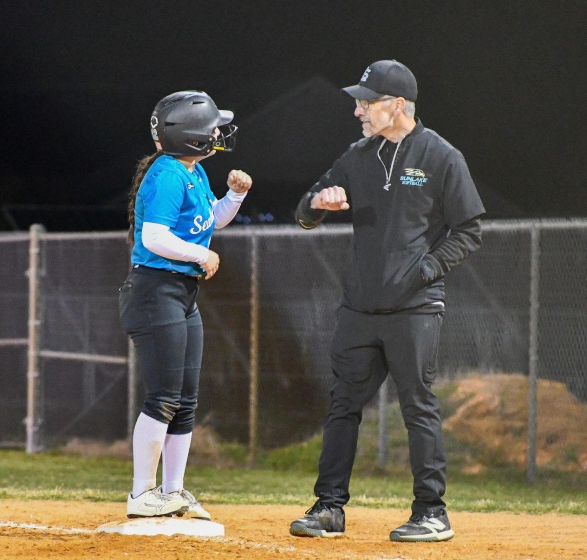 Alondra Arauz Colon stands on base during the game. She shares a quick fist bump with her coach.