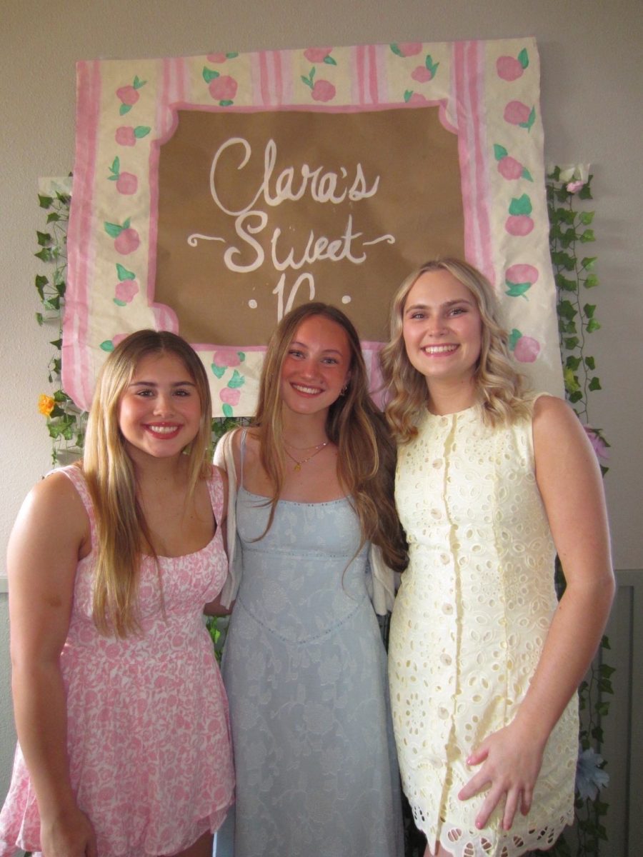 Molly Meier and her friends stand in front of a “Clara’s Sweet 16” sign, smiling for the photo. Wearing their dresses and celebrating, their friend's birthday.